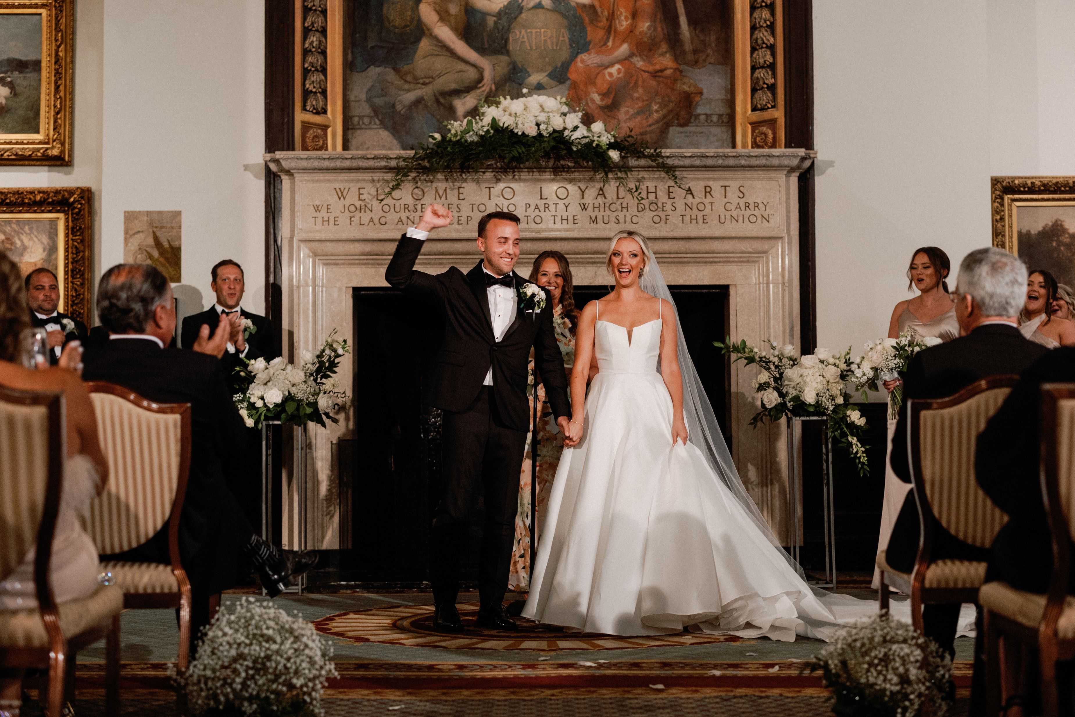 Wedding couple standing in a formal setting with guests and decorative elements.